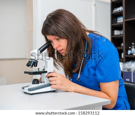 Young woman vet doctor examines the test under the microscope