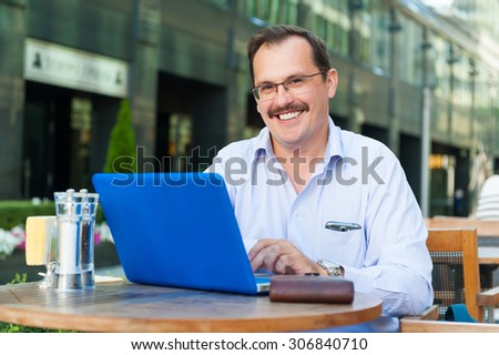 Middle age smiling businessman works on laptop in outdoor cafe