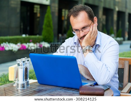 Middle age sad businessman works on laptop in outdoor cafe