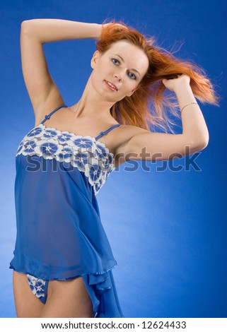 Sexy girl shows her fly-away red hair on the blue background in studio