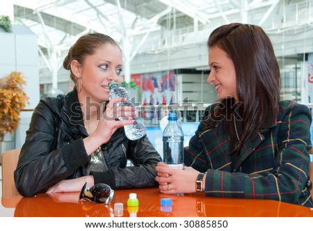Two young girls drink water in food court in a mall