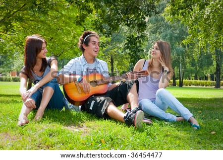 Guy playing guitar in the park, next to him sat two beautiful girls