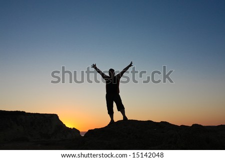 Silhouette of the man with the hands up on mountains on sunset