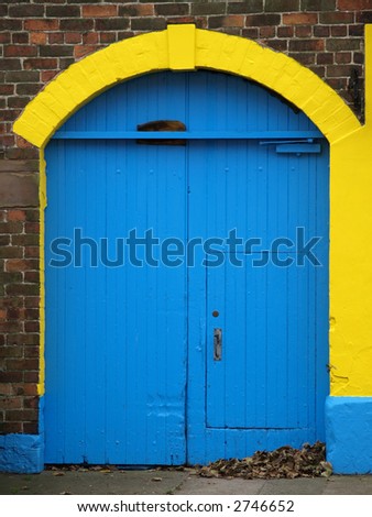Blue painted wooden doors surrounded by a yellow arch in a red brick wall.