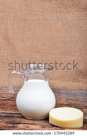 Glass jug with milk and piece of cheese