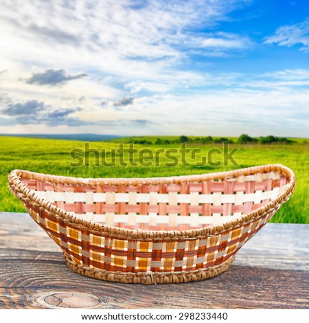Empty basket on old wooden table.Blurred wheat field in the background