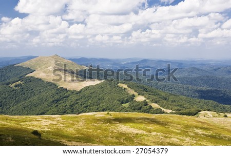 View of green mountain with meadow, blue mountains away and cloudy sky.