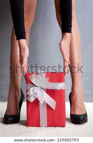 Woman\'s beautiful sexy legs and  Christmas red gift box with silver ribbon and bow
