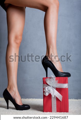Woman's beautiful sexy legs and  Christmas red gift box with silver ribbon and bow