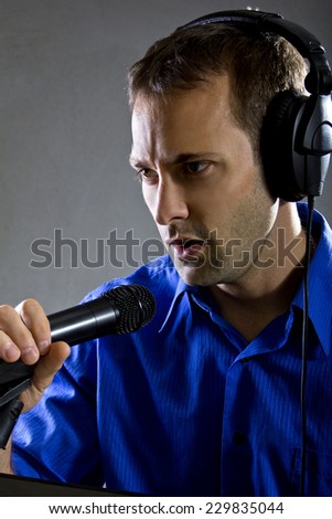 male voice over artist or singer on a microphone wearing a blue shirt on a concrete background