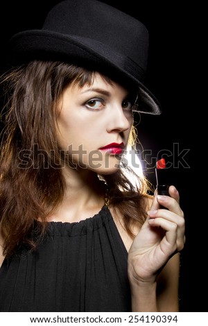 stylish caucasian female putting on red lipstick on black background