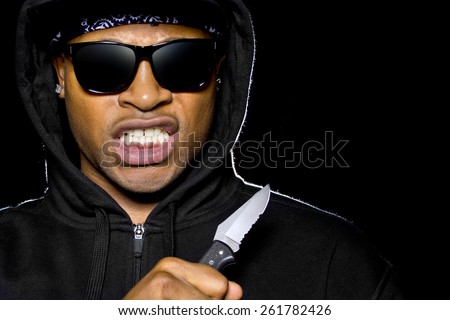 thug wearing a hoodie and holding a knife coming out of the shadows