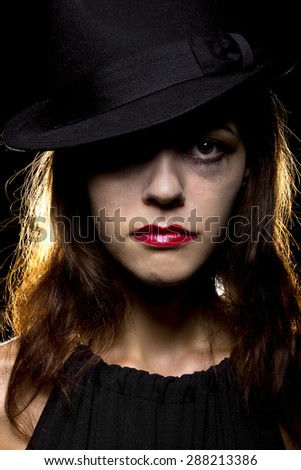 Woman with smeared make-up by crying tears. Noir style.  She is wearing a hat and on a black background.