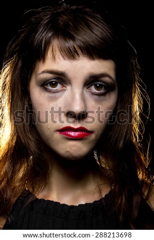 Noir style woman crying.  Her tears have ruined and smeared her make up. She is on a black background.