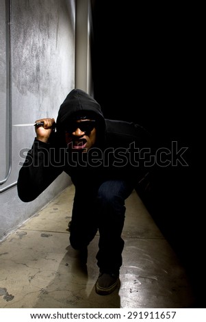 Hooded criminal with a knife hiding in the shadows of a street alley.  He is in a dark alley and partially visible as a silhouette.