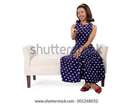 Woman wearing a blue polka dot dress on a traditional chaise furniture.  She is sitting on a vintage chair and her clothing is retro style.