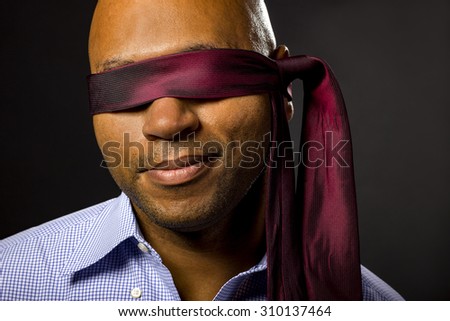 Black businessman blindfolded to represent corporate uncertainty.  The man is disabled by covering his eyes to illustrate vulnerability and employment issues.