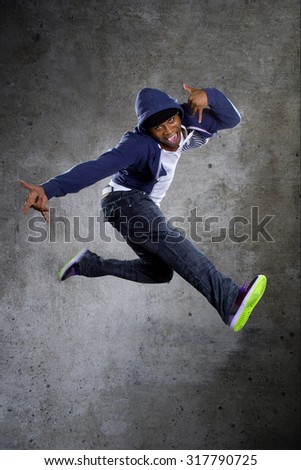 Black urban break dancer wearing a blue hoodie and jumping.  The man is energetic and active.
