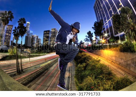 Young black male wearing a blue hoodie jumping in Los Angeles.  The background is the downtown LA freeway.