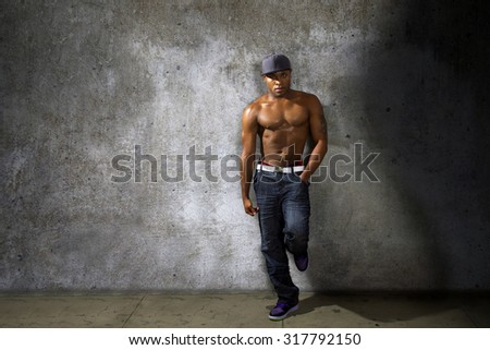 Muscular black man modeling jeans and shirtless torso on urban concrete wall.  The background is a grunge concrete alley wall.