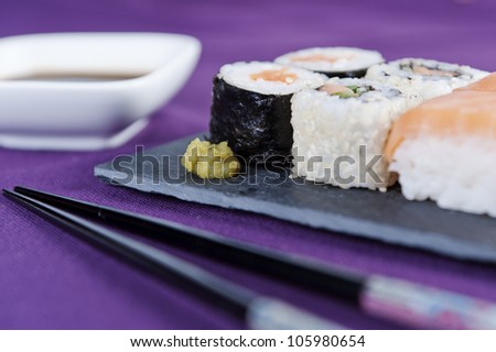 Various kinds of sushi on stone plate with chopsticks and cup soy sauce besides