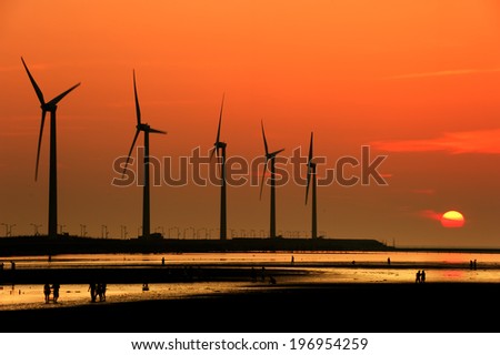 Windmills being observed by several people at sunset.