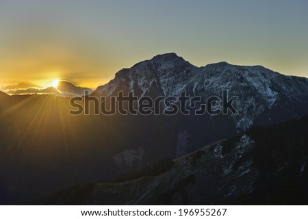 Sun setting behind clouds over the snow capped mountains.