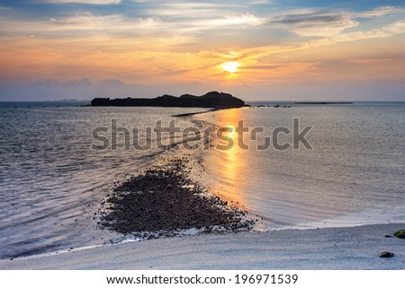 Sun shining through clouds over a body of water around a rock mass.