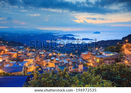 A well lit town situated in hills beside a large body of water.