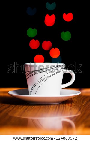 the cup of coffee is photographed on a black background in color patches of light of light
