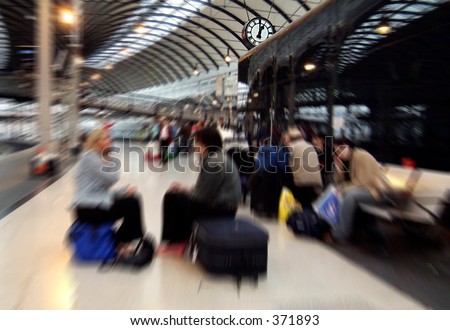 Zoom blurred image of people waiting for trains on Newcastle-upon-Tyne central station, UK, the zoom centred on station clock showing one o'clock 13.00 hrs