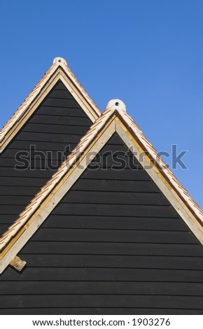 Overlapping triangular roof shapes of restored ancient wooden building against intense clear blue sky.