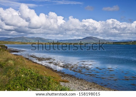 Shoreline on Valentia Island, near the Ring of Kerry, Ireland. A peaceful scene of clean blue water, fluffy clouds in a clear sky and distant mountains.