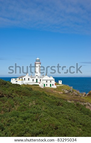 The white painted lighthouse at Fanad Head, Donegal, Ireland stands on a cliff top above the blue Atlantic Ocean, a safety beacon for shipping in the dangerous coastal waters around the rocky shores.