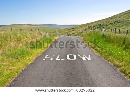 A speed sign painted on a dangerous single track country road in a lonely mountain area reads Slow to warn of hazards to traffic ahead.
