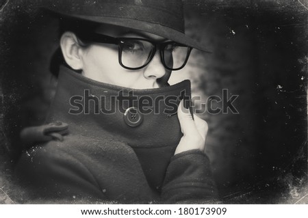 Portrait of a young woman in trench coat, with glasses, hiding the face. Black and white