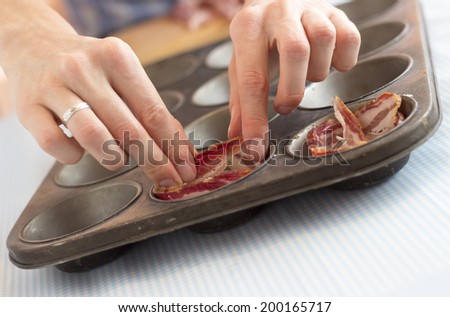 Hands putting bacon into muffin baking pan, making paleolithic muffins for breakfast