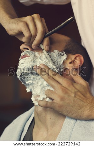 Young man getting an old-fashioned shave at the barber shop. Closeup, retro styled imagery
