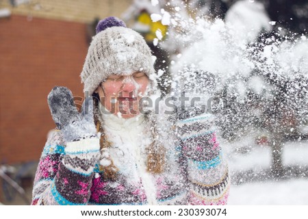 Portrait of a frowning young woman in the middle of a snowball fight getting a snowball in her face