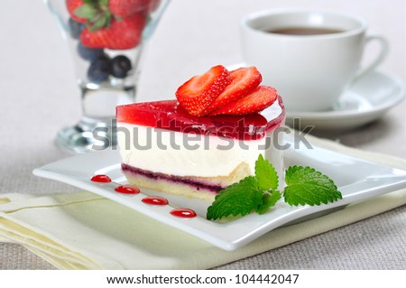 a piece of strawberry cheesecake on white plate with coffee cup and berries in glass