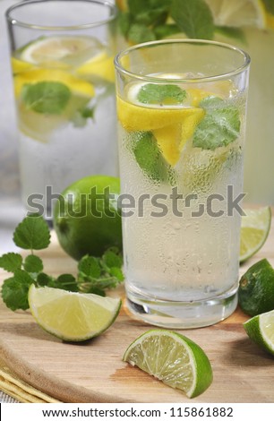 Cold lemonade in glass with ice, lime and lemon on cutting board