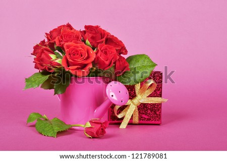 bouquet of red roses in a pink watering can with red gift box on a pink background