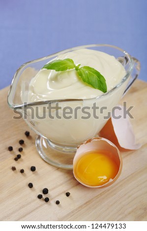 Homemade mayonnaise in a  gravy boat with raw egg on wooden cutting board