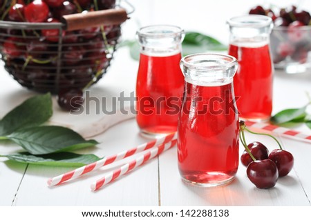 Cherry juice in jars and fresh ripe cherries on wooden background