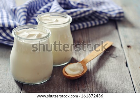 Greek yogurt in a glass jars with spoons on wooden background