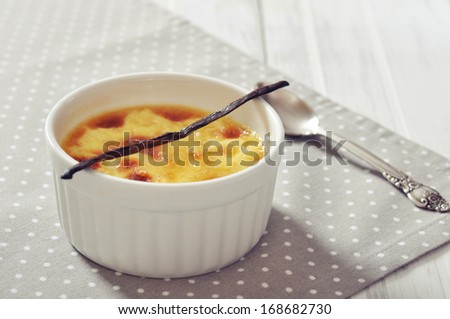 The creme brulee in ceramic baking mold with vanilla pod on wooden table