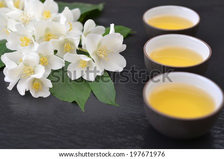 Green tea in cups with jasmine flowers on wet  graphite background