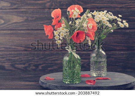 Wildflowers and poppies flowers in vintage bottle  on wooden background