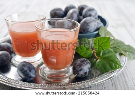 Plum juice in glass with fresh plums on wooden background