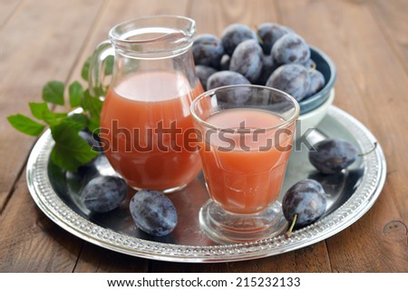 Plum juice in jug and glass with fresh plums on wooden background